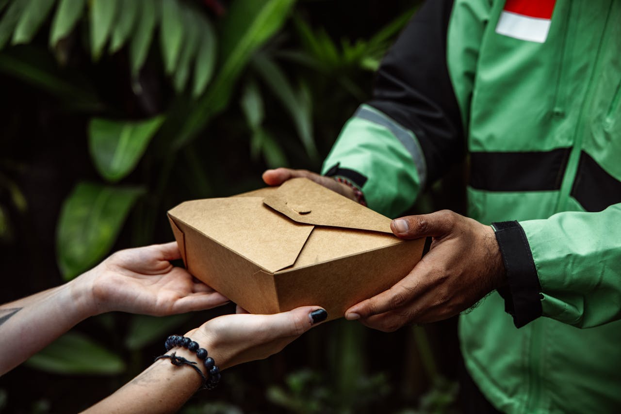 Close-up of hands exchanging an eco-friendly takeout box outdoors.