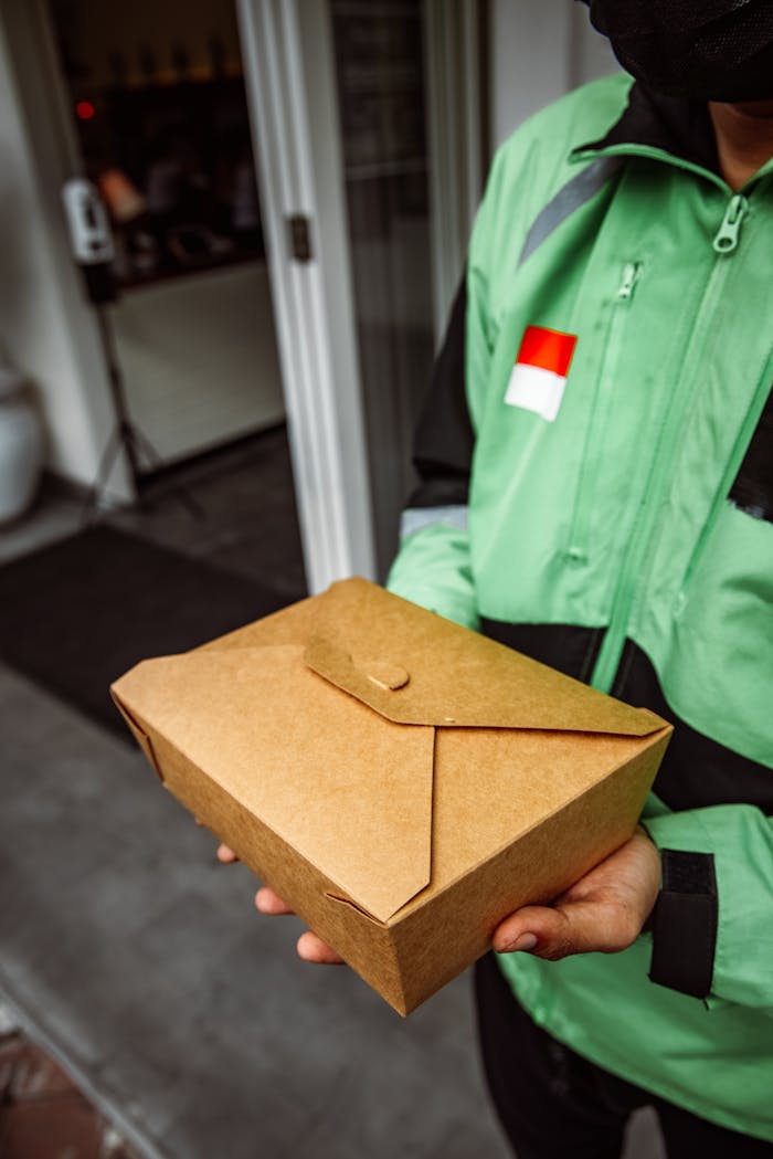 Close-up of a delivery person holding eco-friendly packaging outside a restaurant.
